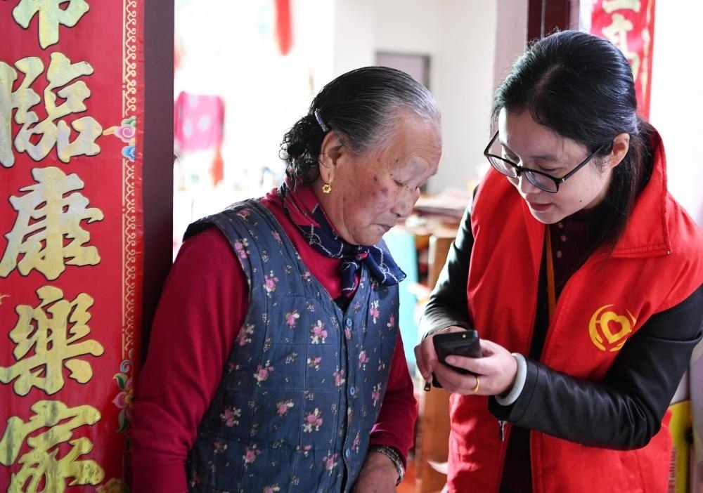在福州市長(zhǎng)樂(lè)區(qū)航城街道籌岐村，智慧養(yǎng)老平臺(tái)派駐社區(qū)的助老員（右）在為老人陳鳳英（左）講解養(yǎng)老定制手機(jī)的用法（2021年11月26日攝）。新華社記者 魏培全 攝