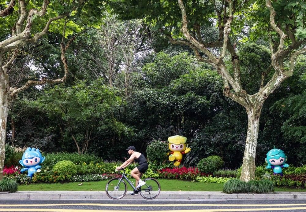 市民在杭州市南山路上一處亞運會主題吉祥物雕塑前騎自行車。