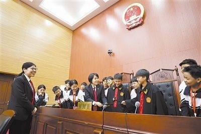 圖③：同學(xué)們穿法袍、敲法槌，爭(zhēng)做“小法官”。
