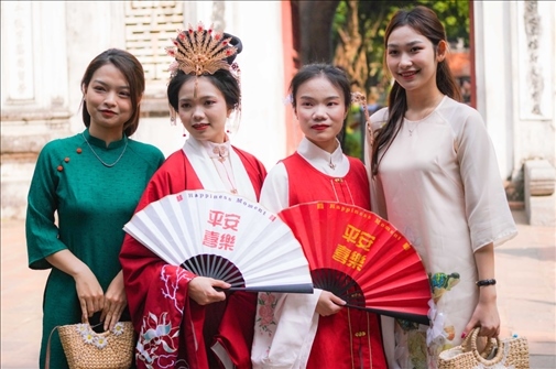 身穿古裝的中國(guó)游客和身穿越南傳統(tǒng)服飾奧黛的越南青年在文廟門前合影。