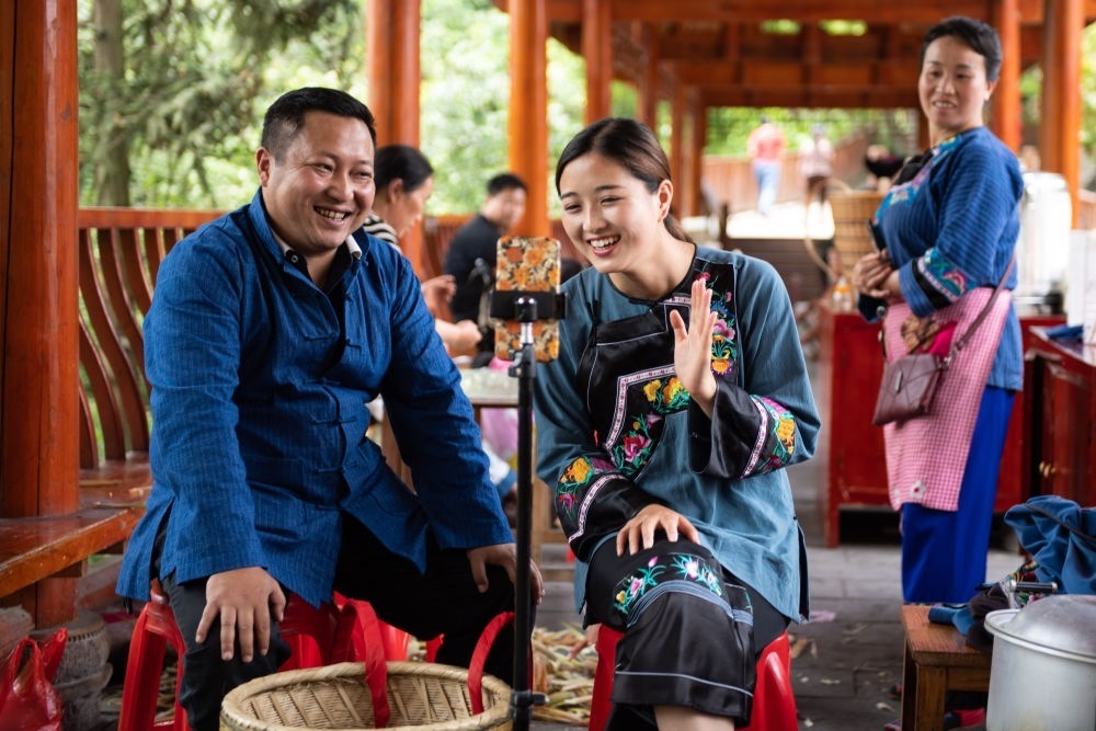 在湖南省湘西土家族苗族自治州花垣縣十八洞村，十八洞村扶貧隊(duì)長(zhǎng)麻輝煌（左）與返鄉(xiāng)大學(xué)生施林嬌（中）一起直播推銷(xiāo)土特產(chǎn)（2020年5月15日攝）。新華社記者 陳思汗 攝