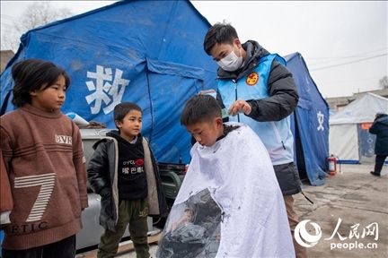 12月22日，在積石山縣大河家鎮(zhèn)大河村安置點，志愿者正在為小朋友理發(fā)。人民網(wǎng)記者 翁奇羽攝