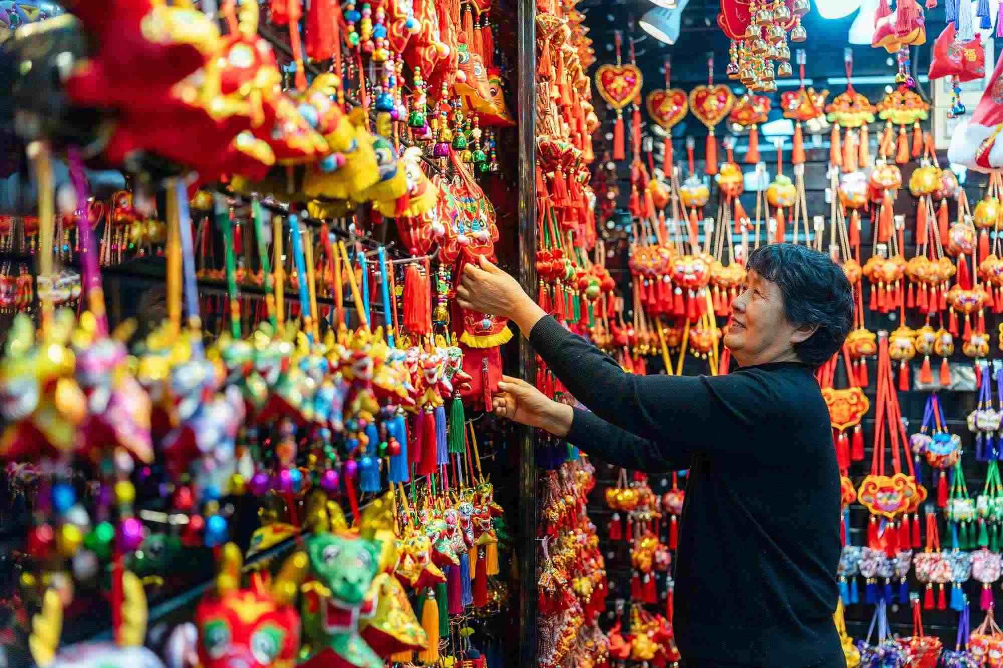 2023年12月11日，金華義烏國際商貿(mào)城，龍年喜慶用品掛滿攤位，顧客正在挑選中。