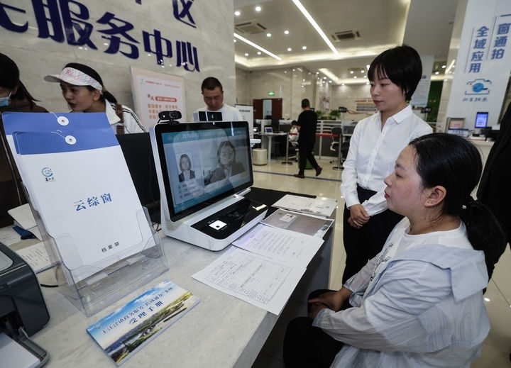 在浙江省嘉興市秀洲區(qū)王江涇鎮(zhèn)便民服務中心的“跨域通辦·云綜窗”窗口，辦理開業(yè)登記的個體工商戶（右一）通過該系統(tǒng)與江蘇省蘇州市吳江區(qū)盛澤鎮(zhèn)行政審批局工作人員視頻連線，進行身份讀取及材料線上審核（2024年5月9日攝）。新華社記者 徐昱 攝