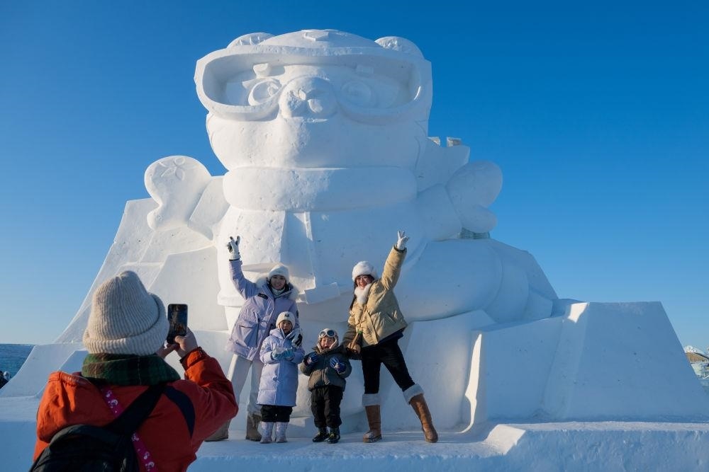 2025年1月3日，在黑龍江哈爾濱冰雪大世界園區(qū)，游客與亞冬會吉祥物雪雕“濱濱”合影
